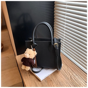 Detail of black lychee grain leather bucket bag with cute teddy bear charm and logo