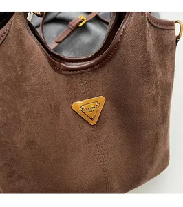 Dettaglio ravvicinato della borsa a secchiello in pelle scamosciata marrone con logo dorato