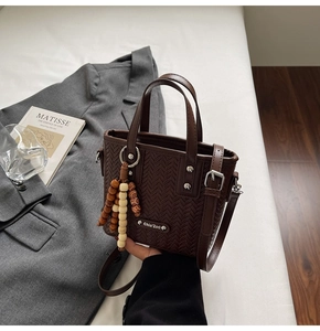 Détail du sac à main marron foncé avec texture tressée, pompon perlé et logo sur bureau
