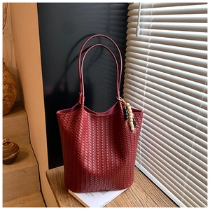 Close-up of wine red woven leather tote bag with stylish beaded pendant detail