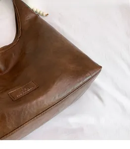Gros plan sur la texture cuir mat marron vintage et l'étiquette d'un grand sac bandoulière
