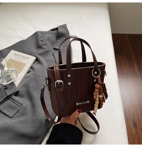 Détail du sac à main marron foncé à texture tissée avec pompon en bois et logo en métal