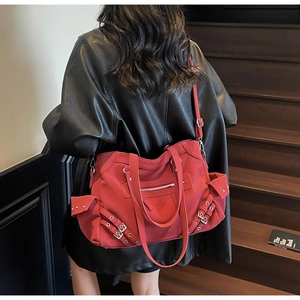 Detail of red large capacity tote bag with metal buckles and adjustable strap on a model