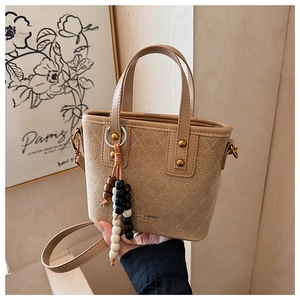 Détail du sac seau en daim kaki avec surpiqûres matelassées et pompon en perles de bois