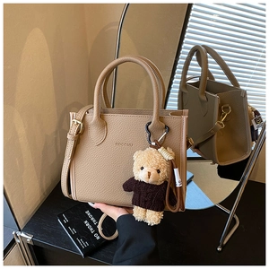 Detail of light khaki pebble leather bucket bag with knitted bear charm and top handle