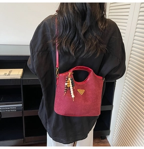 Détail du sac seau en daim bordeaux mat avec breloque perlée bohème et bandoulière amovible