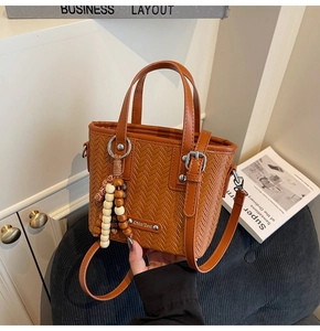 Détail du sac seau tressé caramel avec pompon en perles de bois et logo en métal
