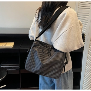 Detail of checkered canvas crossbody bag with black adjustable strap and dual zipper closure