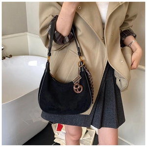 Detailed view of black suede crescent bag featuring gold hardware and quirky charms