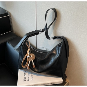 Détail d'un grand sac bandoulière noir avec sangle réglable et pendentif en peluche