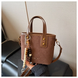 Détail du sac seau en daim marron avec surpiqûres matelassées, rivets dorés et breloque