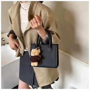 Detail of black lychee grain tote bag with bear charm worn with beige trench coat