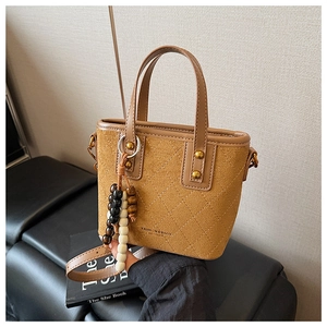 Détail du sac seau en daim caramel avec matelassage en losanges et charms en bois