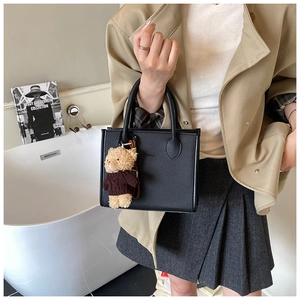Detail of a black textured leather tote bag with a cute teddy bear charm accessory