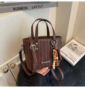 Détail du sac à main marron foncé à texture tressée avec perles rétro et plaque logo