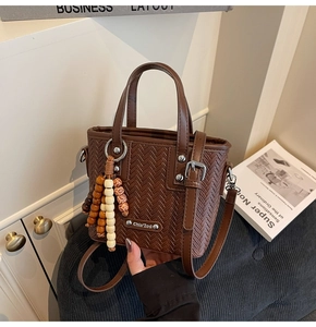 Détail d'un sac seau tressé marron avec pompon en perles de bois et logo métal