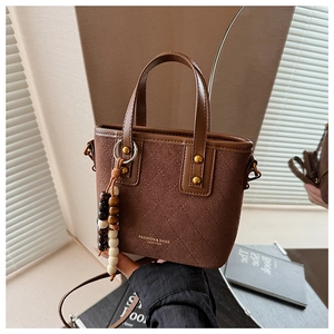 Détail du sac seau en daim marron avec matelassage en losanges et pendentif à perles chic