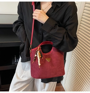 Sac seau en daim rouge avec breloque en bois et longue bandoulière porté par un mannequin