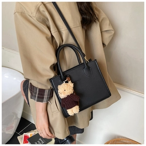 Detailed view of black litchi leather bucket bag with cute bear charm and logo engraving