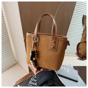 Détail du sac seau vintage en daim marron avec surpiqûres matelassées et breloque perlée