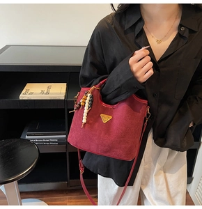 Détail du sac seau bordeaux mat avec breloque en perles de bois et logo triangle doré