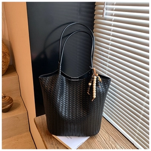Detail of black woven tote bag with wooden bead tassel charm on a wooden surface