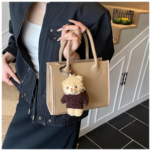 Close-up of beige lychee grain leather tote bag with a cute teddy bear plush charm