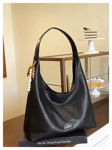 Détail du sac hobo noir mat avec breloque vintage en perles dans un décor de café