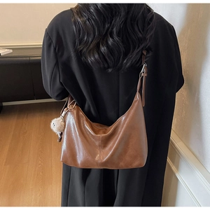 Detail of a brown leather hobo bag with a plush charm and adjustable shoulder strap