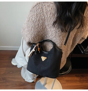 Détail du sac seau noir mat avec plaque dorée triangulaire et pendentif en perles de bois
