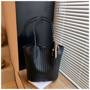 Detail of black woven texture tote bag with wooden bead charm on a wooden table