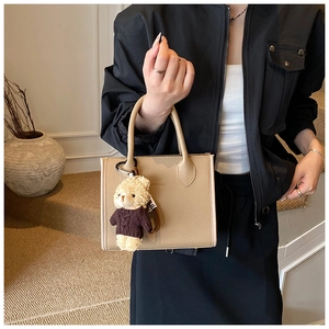 Detail of beige lychee pattern bucket bag featuring a cute purple teddy bear charm