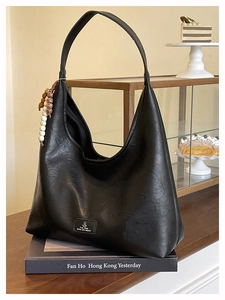 Détail d'un sac hobo en cuir noir avec pompon en perles de bois et étiquette de marque