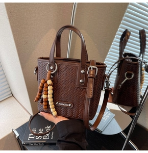 Détail du sac en cuir tressé marron foncé avec pompon en bois et plaque logo argentée