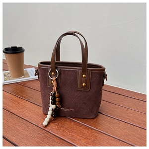 Détail du sac seau en daim rétro avec surpiqûres losanges et pompon en perles de bois