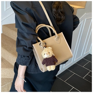 Detail of beige leather bucket bag featuring a round handle and cute teddy bear charm