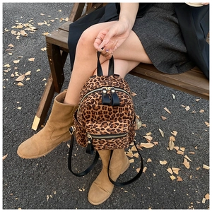 Close-up of a mini leopard print backpack with black leather straps on a wooden bench