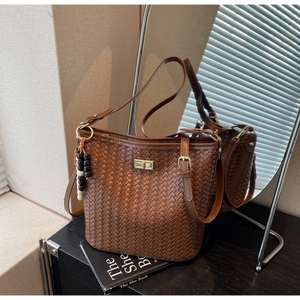 Detail der braunen Web-Eimertasche mit goldenem Drehverschluss und Perlenanhänger-Deko