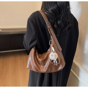 Détail du sac hobo en cuir marron vintage avec large bandoulière et pendentif en peluche
