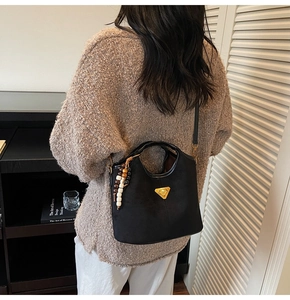 Détail du sac seau noir mat avec logo triangle doré et breloque en perles vintage
