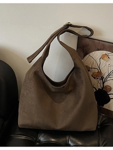 Large coffee brown suede hobo bag with gold buckle on a textured chair in a minimal room