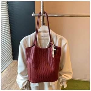 Detail of woven burgundy leather tote bag featuring a retro wooden bead charm accessory