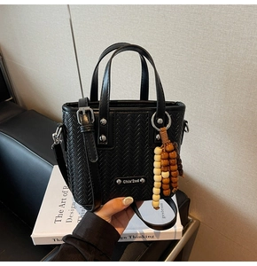 Détail du sac seau noir tressé avec breloque en perles de bois et plaque logo en métal