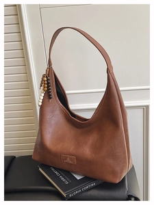 Détail du sac hobo marron mat avec bandoulière large et pompon en perles de bois vintage