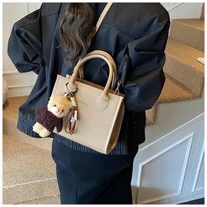 Detailed texture of beige tote bag with cute bear charm and thin shoulder strap