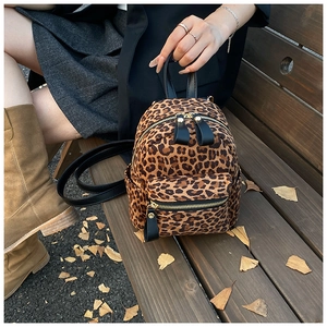 Mini leopard print backpack with gold hardware and leather straps on an outdoor bench