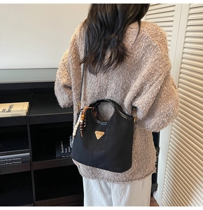 Détail d'un sac seau noir mat avec plaque dorée et pendentif en perles de bois colorées