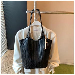 Detail of black woven tote bag with wooden bead charm hanging on a white blazer coat