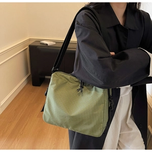 Detail of green checkered canvas crossbody bag with adjustable strap and buckle closure