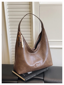Détail d'un sac hobo en cuir marron avec gland à perles vintage et patch logo brodé